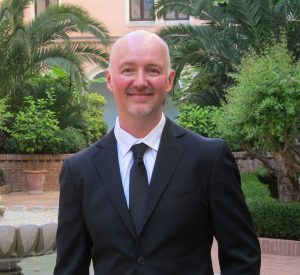Dave Lackie in a black suit, standing in a beautiful Italian park